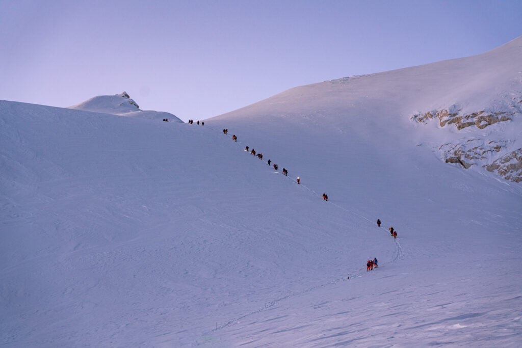 a group of people walking up the side of a snow covered mountain