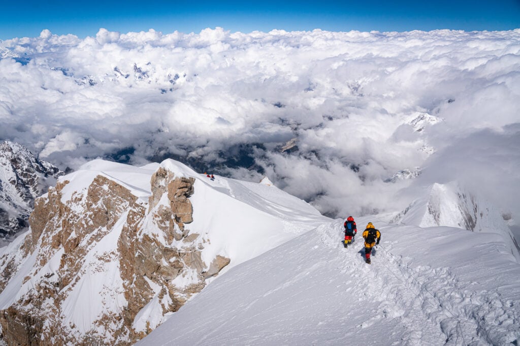 a couple of people walking up the side of a snow covered mountain