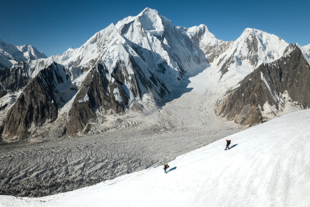 a couple of people riding skis down a snow covered slope