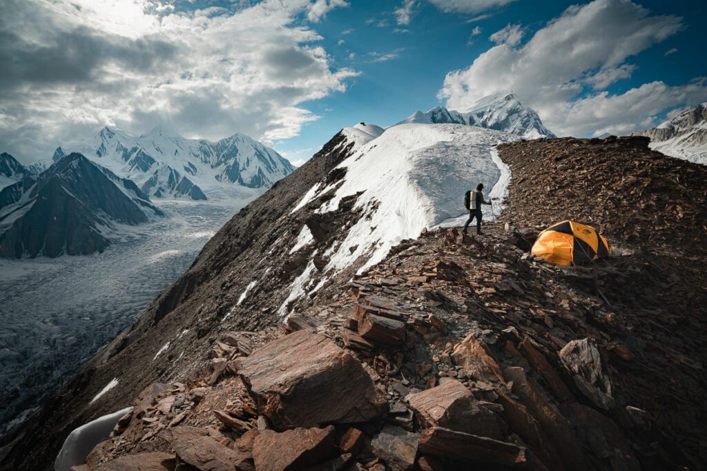 a man standing on top of a mountain next to a tent