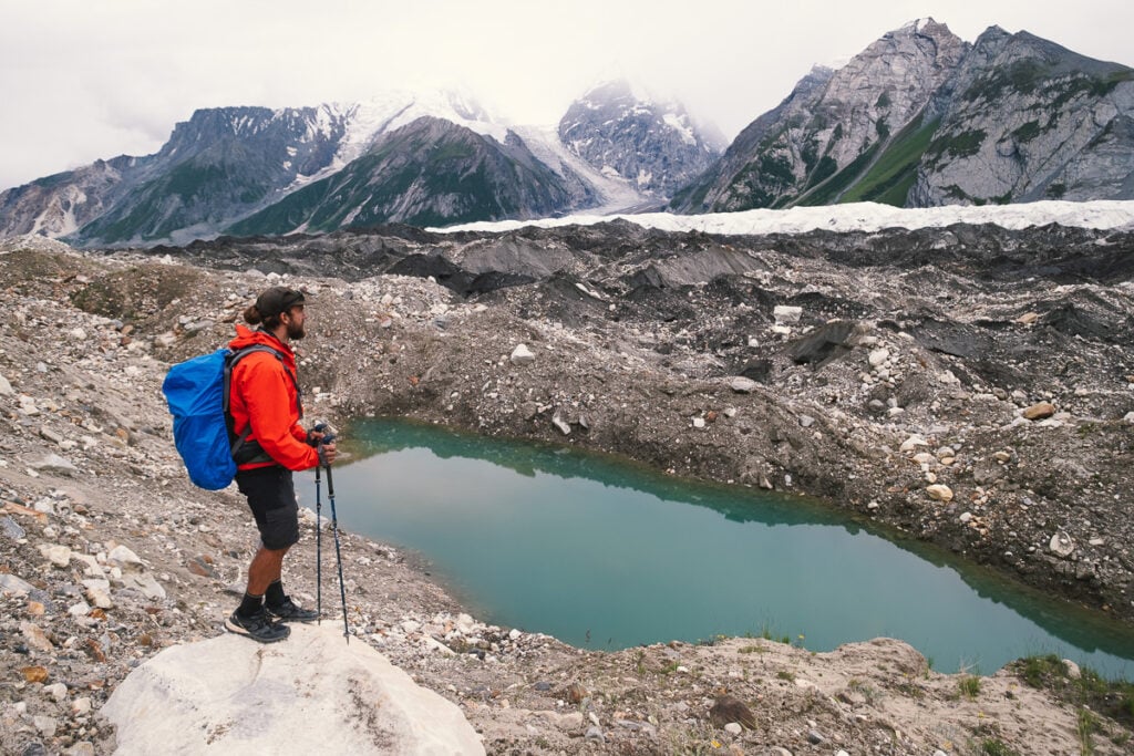 a man with a backpack and skis stands on a rock near a body of