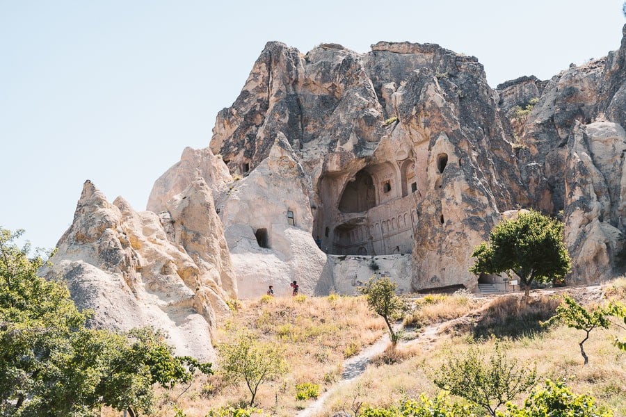 a group of people walking up a hill next to a cave.